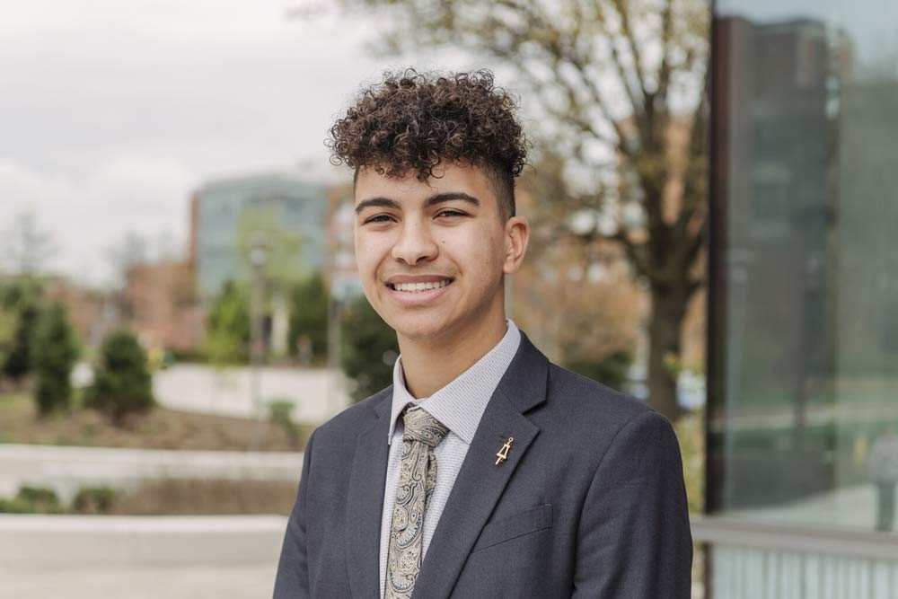 A three quarters portrait of a young undergraduate researcher standing outside in a courtyard